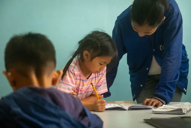 A teacher leaning in to help a student at the table